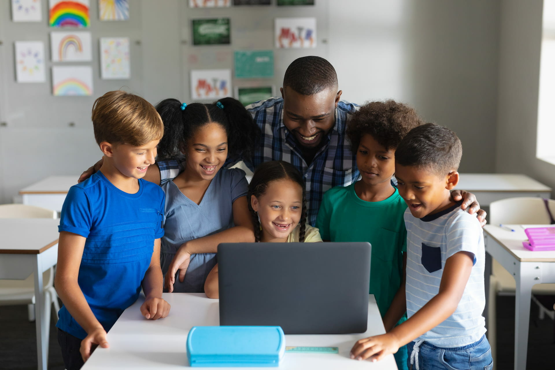 elementary students around a laptop computer with their African american young male teacher